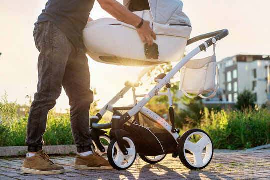 A young father lays out a stroller before walking with the baby. A man holds a cradle with a baby in his hands
