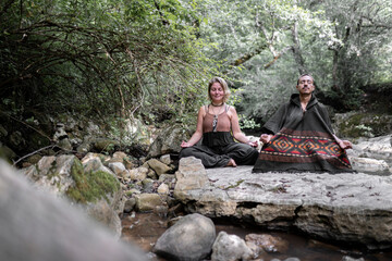 Naklejka na ściany i meble A young couple is meditating in a river sitting on a rock