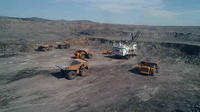Group of technological transport around huge mining excavator. Aerial view dump trucks and small loader