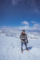 portrait of young man looking at camera while standing at the top of snowy mountain
