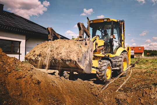 Excavator working at house construction site - digging foundations for modern house. Beginning of house building. Earth moving and foundation preparation.