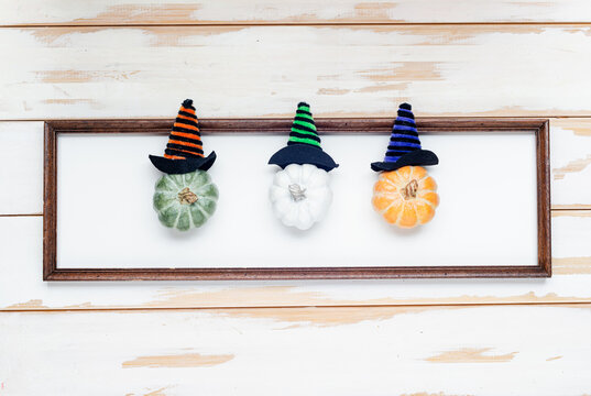 colored pumpkins in halloween hats in photographic frame   on wooden white background of boards, autumn holiday concept. View from above