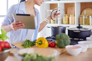 Young woman using a tablet computer to cook in her kitchen.