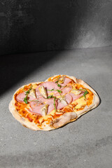 Italian pizza with ham and artichokes on dark background. Ham pinsa on gray stone table with hard shadow. Roman pizza with ham and artichokes on concrete background. Pinsa menu.
