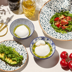 Italian salad with burrata cheese and vegetables on sunny day. Aesthetic composition with burrata and mozzarella cheese with tomato salad and sliced avocado. Summer lunch with burrata salad, tomatoes.