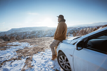 portrait of a man enjoying the view of cappadocia in winter sitting at the front of his car