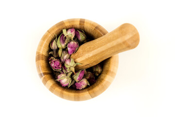 Dehydrated pink rose buds in a wooden mortar and pestle top down view isolated over white