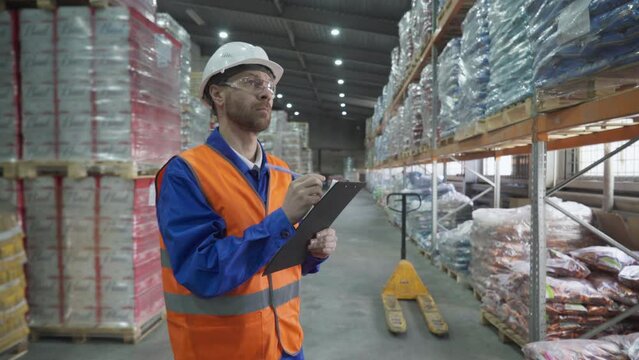 Storehouse manager worker ticks off inventory items in the checklist. Warehouse manager counting up the stocked inventory supply using the checklist. Manager inspecting the inventory with a checklist