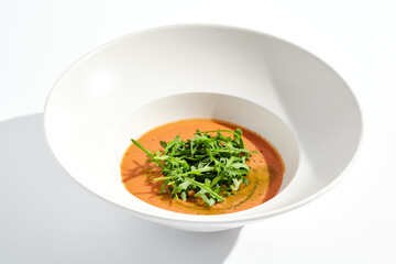 Summer Spanish soup - gazpacho with rocket salad isolated on white background. Vegetarian cold tomato soup in white plate. Meatless food in menu. Veggie lunch. Healthy food. Plant based eating.