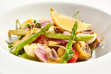 Classic Nicoise salad with grilled tuna, potatoes, asparagus, tomatoes and olives with mustard dressing. French cuisine - Tuna salad with vegetables, eggs and vinaigrette sauce in white background.