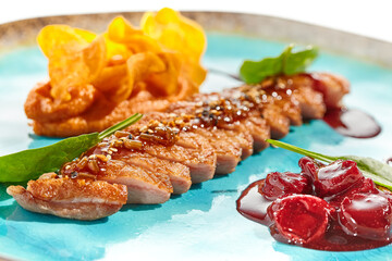 Roast duck breast with batata chips and cherry sauce isolated on white background. Delicious dinner - cooked duck meat with berry jam and sweet potato chips on trendy plate. Contemporary cuisine.
