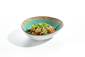 Pan asian food - chicken udon with mushrooms on white background. Noodle with chicken  on wok in asian style. Indonesian wok with black udon noodles and chicken in ceramic bowl.