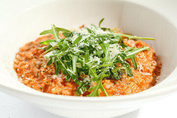 Vegan tomato risotto with ruccola on white plate. Italian dish - veggie risotto isolated on white background. Plant based dining. Clean eating in restaurant menu. Eat less meat. Vegetarian lunch.