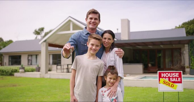 Happy family buying a house, holding a key while standing outside together. Smiling, cheerful home owners ready to relocate, excited to move in and give their children a secure, safe family home