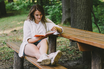 Woman holds book in her hands. Reading the book sitting on a bench at outdoors