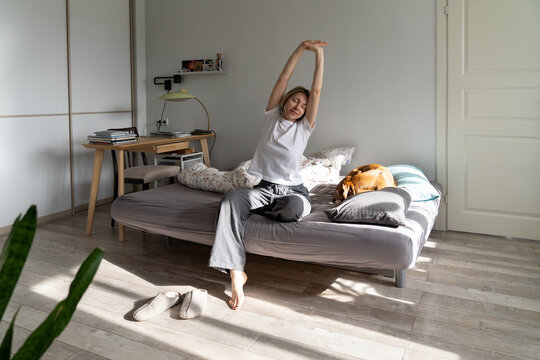 Middle-aged female in pajamas stretches out hands. Half-awake lady does warm-up stretching muscles o