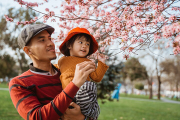 happy father and daughter looking at cherry blossom in the park