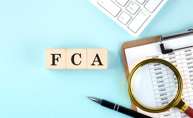 FCA word on wooden cubes on blue background with chart and keyboard