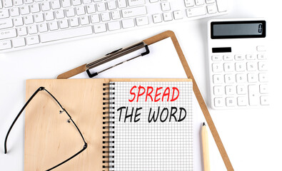 Notebook with the word SPREAD THE WORD with keyboard and calculator on the white background