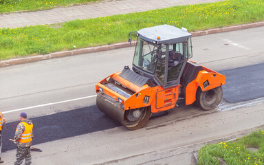 Road works on asphalt laying. Workers in vests are laying patches and rolling them out with a large roller.