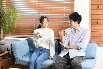 屋内でカップを持ち会話する若いカップル