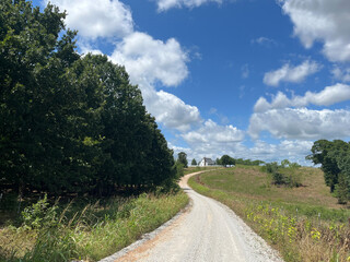 Fototapeta na wymiar Farmhouse in the distance and gravel road curving through a rural area.
