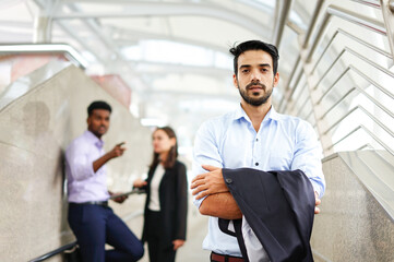 young executive standing with arms crossed, background are employee talking about him as bullying....