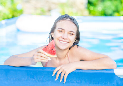 Smiling teen girl eats watermelon in the pool at sunny day