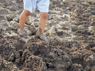 Dirty bare foot child with mud in nature background. Kid playing in mud pit outdoor. Concept of learning nature, fun freedom playing, family activity outdoor, ef learning, skin health care.