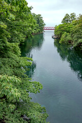Fototapeta na wymiar A red bridge over a clear river flowing into a lake