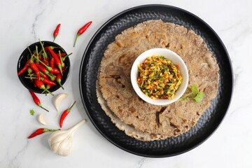 Super spicy green and red bird eye chili chutney using lal and hari mirch, garlic cloves, and coriander. served in a white bowl. Also known as Thecha in Marathi served with Raagi roti. copy space