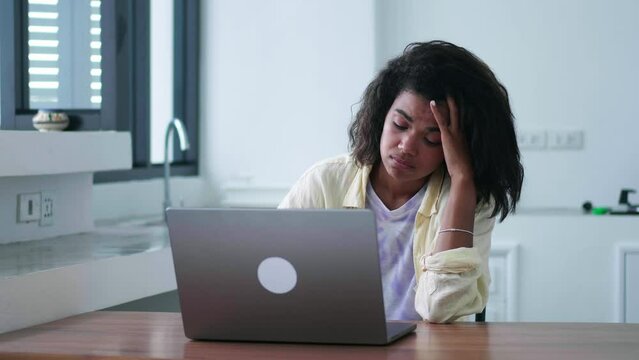 Tired, bored, exhausted woman working on laptop, having difficulties for achieving work and fixing problems, looking aside, with despair from failing planned project while working remotely from home