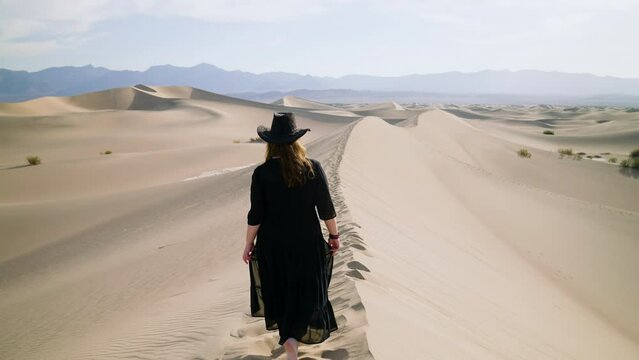 Woman In Black Dress Walking On Top Of Sand Dune In The Death Valley National Park In California, USA - tracking shot