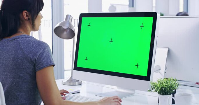 Business woman typing on CGI green screen computer monitor, working in modern office. Female freelancer researching information on mockup PC with chroma key, copyspace and tracking markers at a desk.