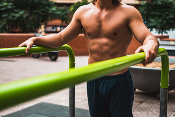 Close up of a non recognizable shirtless muscular caucasian man exercising calisthenics in outdoor bars.