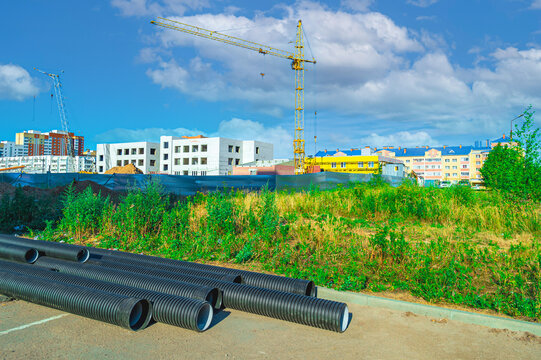 Composite sewer pipes or water pipes for supplying utilities at a construction site, with tower cranes constructing a new building. Reconstruction, installation,  repair of water supply, sewerage.