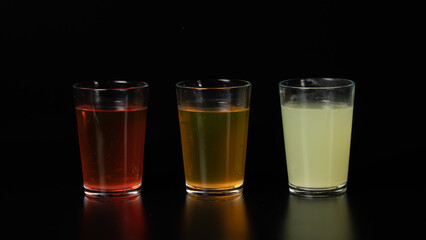 Three glasses of colored water, drinks, juices and cocktails on a black background