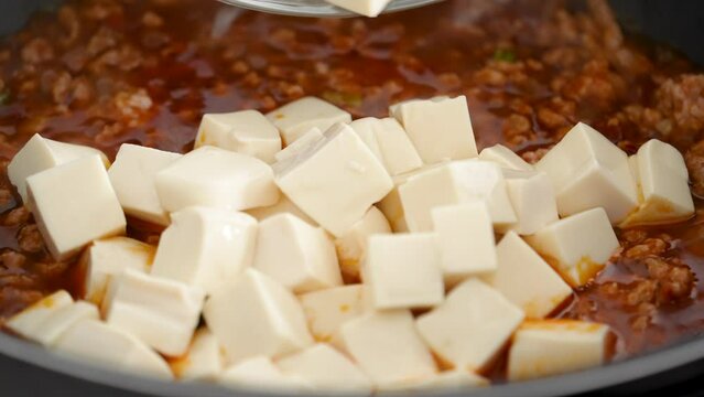 Cooking mapo tofu. Stir-frying tofu with hot spicy sauce in a pot at home.