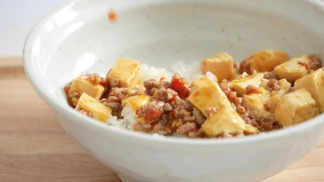 Pouring stir-fried mapo tofu with hot spicy sauce over white rice in a bowl at home