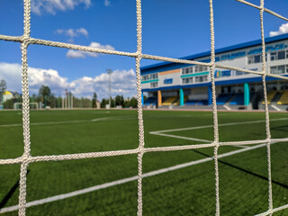 Noyabrsk, Russia - July 17 2022: View of the Noyabrsk sports stadium and a football field with bright green grass through the security net on a sunny summer day against a blue sky. Selective focus