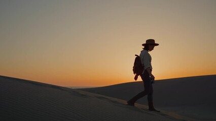 Attractive photographer walking on sand dune at sunset