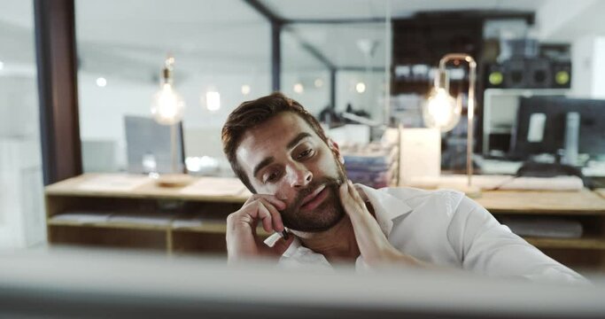 Stressed busines man talking on phone call, looking worried and tense in modern office. Young professional with anxiety, feeling concerned while looking at computer and working overtime on a project