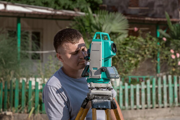 A surveyor with a total station at work on a sunny day. Portrait of a young man next to a total station in the open air. A male construction worker on an open construction site.