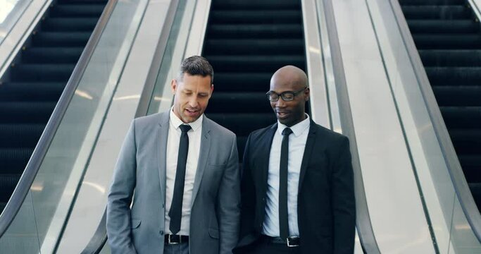 Smiling diverse businessmen on escalator standing, talking and coming down, on their way to conference. Professional, formal and cheerful businesspeople traveling through the convention centre.