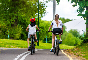 A boy and a girl ride bicycles in a city park