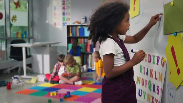 Cute African-American preschool girl write on white board in kindergarten