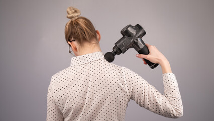 Caucasian business lady makes herself a back massage with a massager gun on a white background.