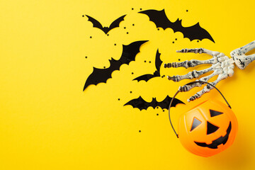 Halloween concept. Top view photo of skeleton hand holding pumpkin basket with bats flying out and...