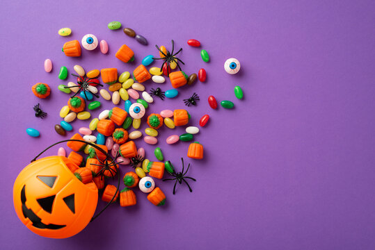 Halloween Concept. Top View Photo Of Pumpkin Basket With Candies Eyes And Spiders On Isolated Violet Background