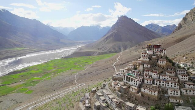 Aerial Drone moving wide shot of a Kee Gompa or Key Monastery over a peak of mountain with a beautiful landscape view of hilly region against clear blue sky in a daylight Spiti valley, India.